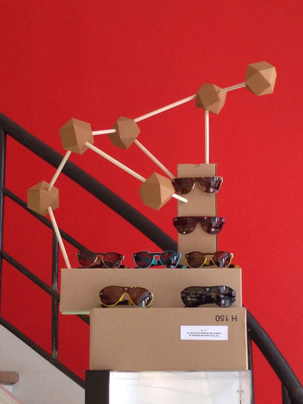 Présentoir en forme de molécule géante en carton et en balsa sur lequel sont posées des paires de lunettes en carton. 