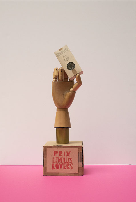 Trophées avec une étiquette prix lentilles lovers avec une main en bois qui tient un paquet de lentilles du Puy. Design les soeurs siamoises.