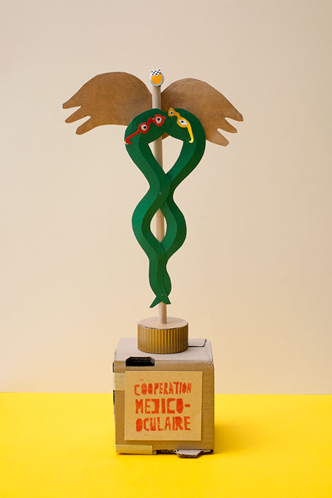 Trophées avec le texte coopération médico-occulaire, deux serpents à lunettes en cartons sont entrelacés évocation du caducée. 